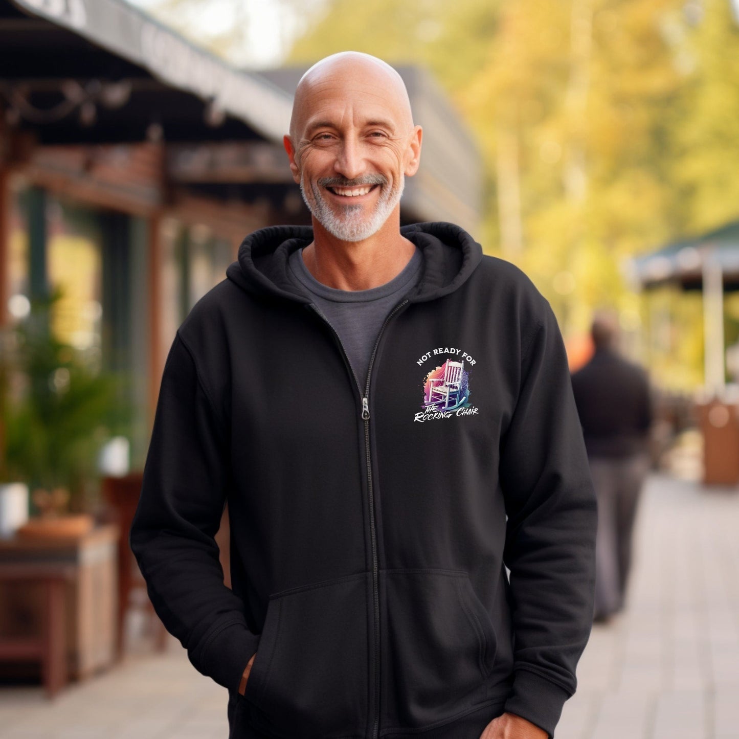 a smiling man in a black hoodie stands on a sidewalk